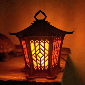 May include: A decorative lantern with a black metal frame and a warm orange glow emanating from the inside. The lantern has a geometric design with intricate cutouts.