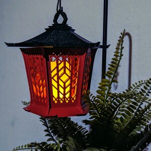 May include: A red and black lantern with a decorative, geometric design. The lantern has a warm, glowing light inside.