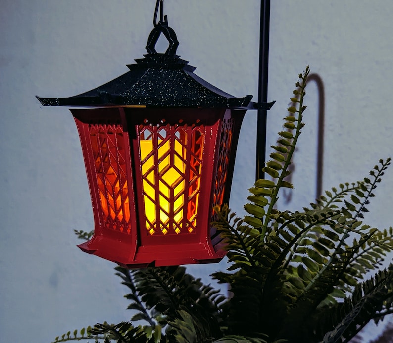May include: A red and black lantern with a decorative, geometric design. The lantern has a warm, glowing light inside.