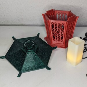 May include: A set of three 3D printed decorative pieces. The largest piece is a red hexagonal lantern with a lattice design. The second piece is a green hexagonal top with a textured surface. The smallest piece is a white rectangular candle holder.