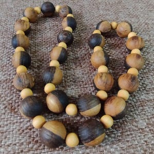 May include: A necklace composed of alternating large spherical beads and small round beads. The large beads feature a two-tone design with dark brown and light tan wood grain, while the smaller beads are a solid, smooth, light yellow colour.