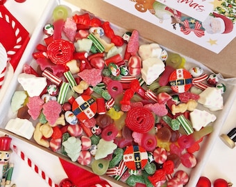 May include: A box overflowing with a colorful assortment of Christmas-themed candies. The candies include red, green, and white sweets, including gummy shapes, hard candies, and wrapped treats. A festive card with "Merry Christmas" is visible.