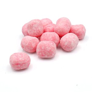 May include: A cluster of pink, round candies with a textured, slightly rough surface. The candies are a light pink color and appear to be coated. The image is set against a plain white background.