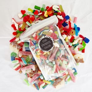 Pode incluir: Um saco de plástico transparente cheio de uma variedade de doces de goma coloridos. O saco é etiquetado com "The Sweetz Club".