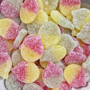 May include: A close-up of a bowl filled with yellow and pink candy. The candy is shaped like small, flat pears and is covered in a fine, white sugar coating.