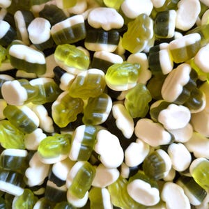 May include: A close-up shot of a pile of gummy candies in various shapes. The candies are primarily green and white, with some resembling frogs and others having a layered appearance. The candies are scattered, creating a textured and colorful display.