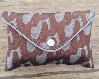 May include: A rectangular envelope-style pouch featuring a brown and light grey abstract pattern. The flap is secured with a single white circular snap button and is finished with a light grey piped edge along the triangular closure.