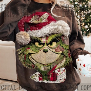May include: Brown sweatshirt featuring a detailed embroidered Grinch face with a Santa hat and scarf. The Grinch has green fur, a mischievous grin, and is wearing a red and white hat. The sweatshirt is a festive holiday design.