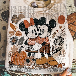 May include: A folded, cream-coloured sweatshirt featuring a graphic of Mickey and Minnie Mouse embracing, with a pumpkin and autumn foliage. The design includes the text "DIGITAL DOWNLOAD" and "LOOKINGFORHERE".