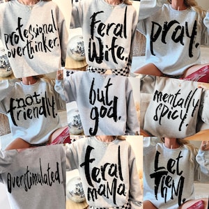 May include: A set of ten gray sweatshirts with black text. The text on the sweatshirts includes "professional overthinker", "feral wife", "pray", "not friendly", "but god", "mentally spicy", "overstimulated", "feral mama", and "let them".
