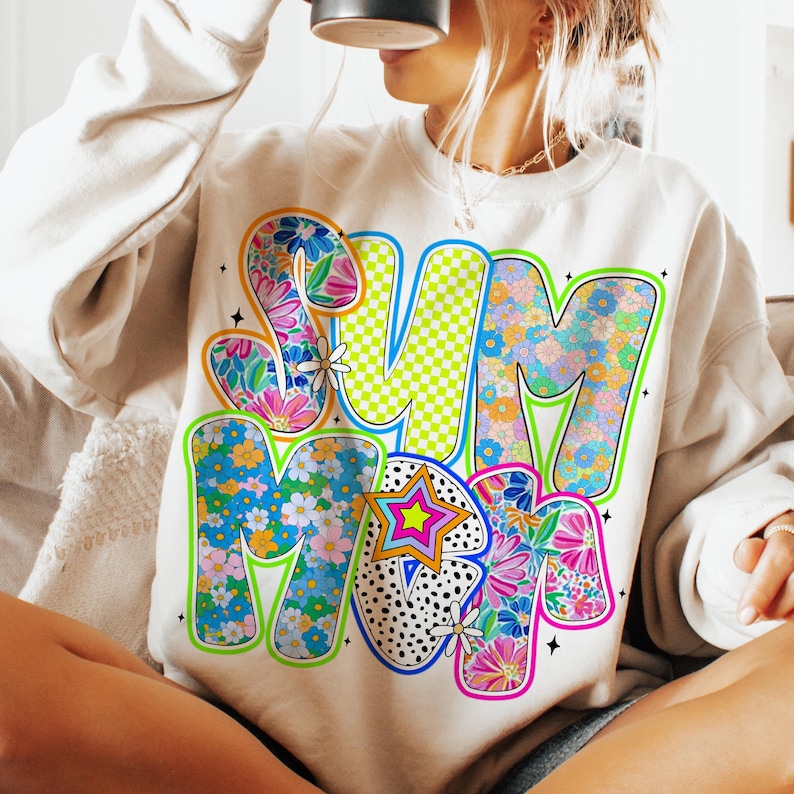 May include: A white sweatshirt with a colorful graphic design that says "Summer" in a retro style. The letters are filled with floral patterns and outlined in neon colors.