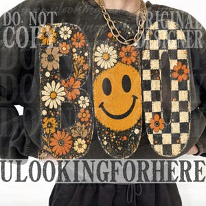 May include: A charcoal gray sweatshirt featuring a large graphic print that spells BOO. The letter B is filled with orange and cream flowers, the letter O is a yellow smiley face with flowers, and the second O has a black and white checkerboard pattern.