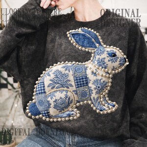 May include: Dark grey sweatshirt with a large appliquéd rabbit design. The rabbit is made from blue and white patterned fabric, and decorated with faux pearls. The sweatshirt has the text "ORIGINAL DESIGNER" printed on it.