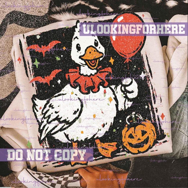 May include: A light-colored sweatshirt featuring a graphic print of a white duck wearing a red ruffled collar. The duck holds a red balloon and a jack-o'-lantern. The background is black with orange bats and small stars. The text ULOOKINGFORHERE is visible.