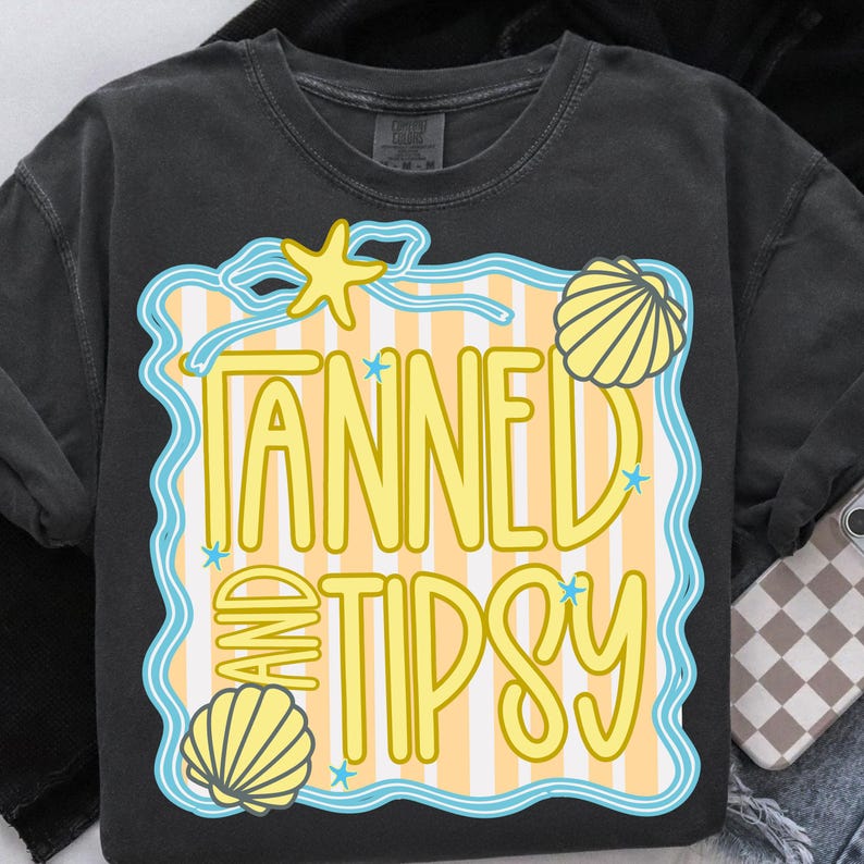 Puede incluir: Camiseta gris oscuro con un dise&ntilde;o amarillo y azul que dice "Tanned and Tipsy". El dise&ntilde;o incluye una estrella de mar, conchas marinas y un fondo a rayas, evocando un tema de playa.