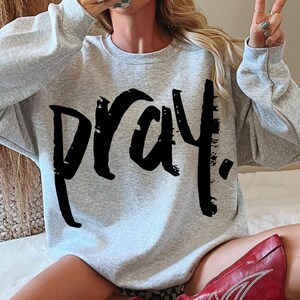 May include: A gray sweatshirt with a black graphic print of the word "pray" in a bold, brushstroke style.