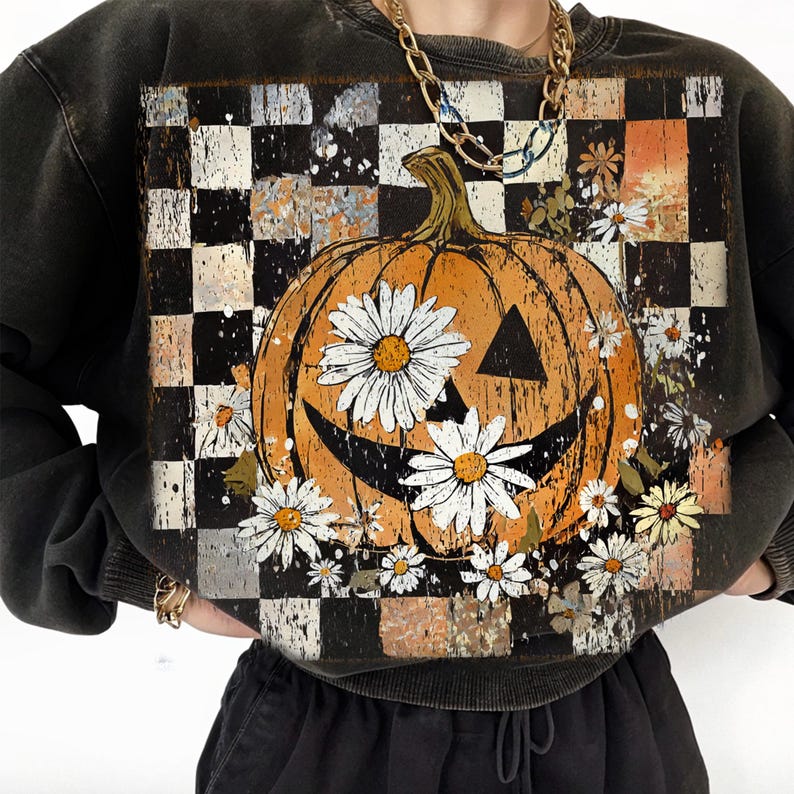 May include: Black sweatshirt featuring a Halloween-themed design. The graphic includes a smiling orange pumpkin with daisy flowers against a checkered background. The sweatshirt has a vintage, distressed look.