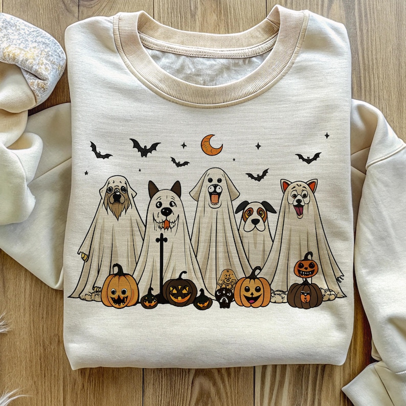 Pu&ograve; includere: Felpa color crema con un design di Halloween. La grafica mostra sei cani vestiti da fantasmi, con zucche, pipistrelli, una luna crescente e stelle. La felpa ha un colletto e polsini beige.