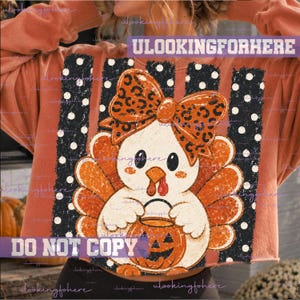 May include: A rust-colored long-sleeve sweatshirt featuring a graphic of a cartoon turkey wearing a leopard print bow and holding a jack-o'-lantern. The design includes black vertical stripes with white polka dots and the text ULOOKINGFORHERE.