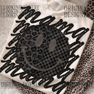 May include: Cream-colored t-shirt with a large smiley face design. The smiley face is split, with one half featuring a leopard print and the other a checkered pattern. The words "Mama" are written in a black, scribbled font around the smiley face.