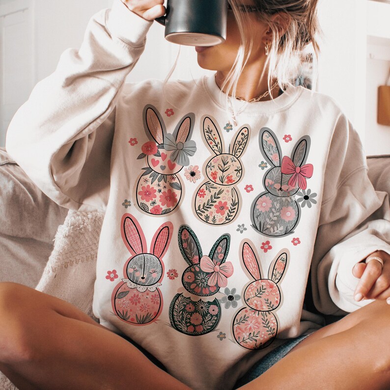 May include: A white sweatshirt with a floral bunny rabbit design. The bunnies are pink, gray, and green with floral patterns.