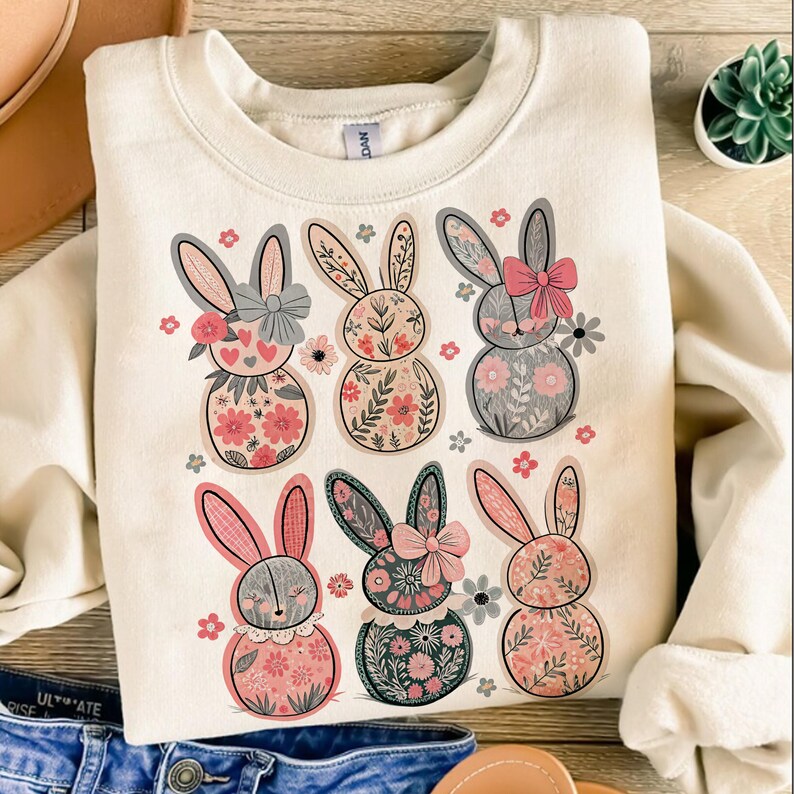 May include: A cream-colored sweatshirt with a graphic of six floral bunny rabbits. The bunnies are all different colors and have different floral patterns. The sweatshirt is a great gift for anyone who loves bunnies or floral patterns.