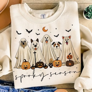 Pu&ograve; includere: Felpa color crema con un design a tema Halloween. La grafica presenta cinque cani vestiti da fantasmi, zucche, pipistrelli, una luna crescente e le parole "spooky season" in nero. Un design festoso e divertente.