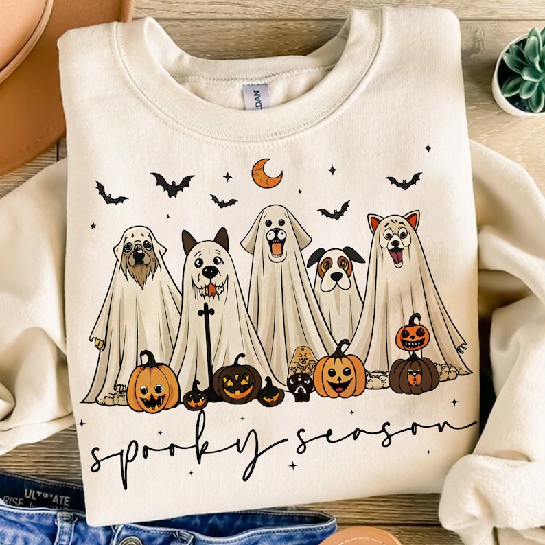 Pu&ograve; includere: Felpa color crema con un design a tema Halloween. La grafica presenta cinque cani vestiti da fantasmi, zucche, pipistrelli, una luna crescente e le parole "spooky season" in nero. Un design festoso e divertente.