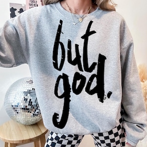 May include: Gray sweatshirt with the text "but god" printed in black.