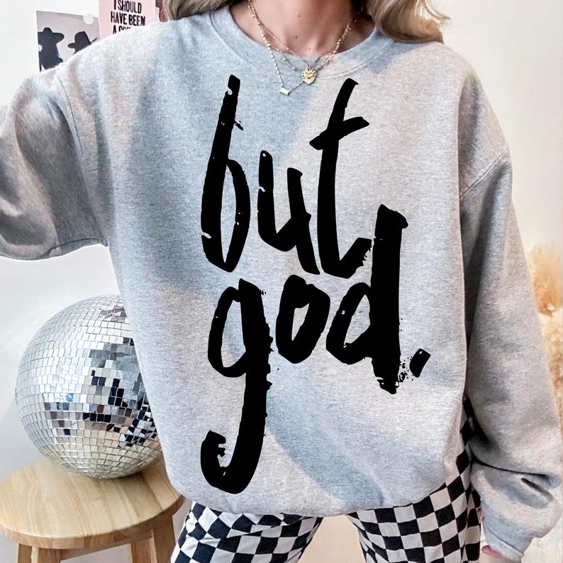 May include: Gray sweatshirt with the text "but god" printed in black.