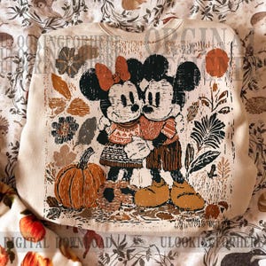 May include: Cream-coloured sweatshirt with a distressed print of Mickey and Minnie Mouse hugging, set against autumnal leaves and a pumpkin. The design uses orange, brown, and green tones, evoking a cosy autumn feel.