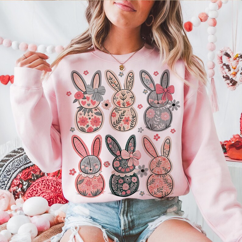 May include: Pink sweatshirt with a floral pattern of six bunnies wearing bows. The bunnies are in a row, with three on top and three on the bottom. The sweatshirt is a crew neck style with long sleeves.