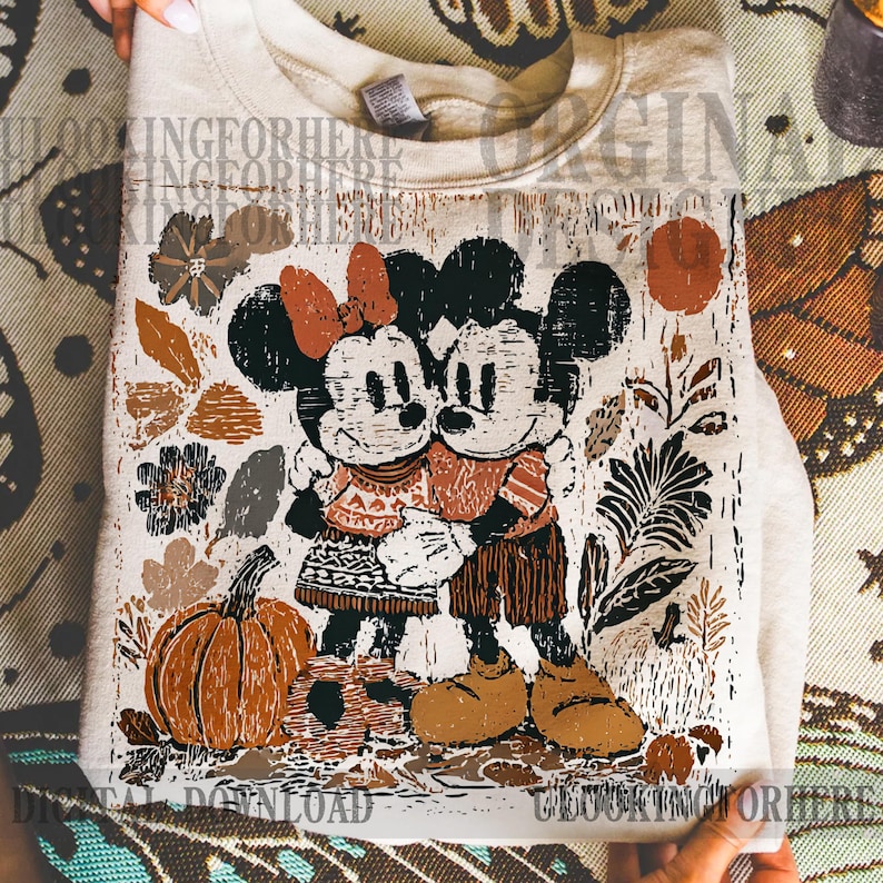 May include: A folded, cream-coloured sweatshirt featuring a graphic of Mickey and Minnie Mouse embracing, with a pumpkin and autumn foliage. The design includes the text "DIGITAL DOWNLOAD" and "LOOKINGFORHERE".