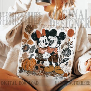 May include: Cream-coloured sweatshirt featuring a graphic of Mickey and Minnie Mouse embracing, with a pumpkin and autumn foliage design. The design includes the text "ORIGINAL DESIGNER" and "DIGITAL DOWNLOAD".