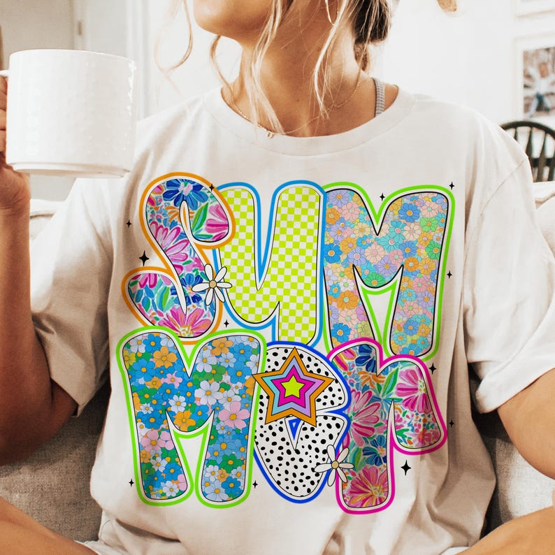 May include: A white t-shirt with a colorful graphic that says "Summer" in a retro style. The letters are filled with floral patterns and outlined in neon colors.