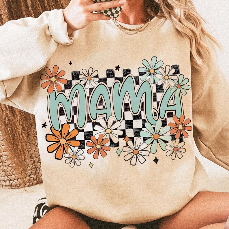Puede incluir: Una sudadera beige con un patr&oacute;n a cuadros y la palabra "MAMA" en una fuente retro rodeada de flores coloridas.