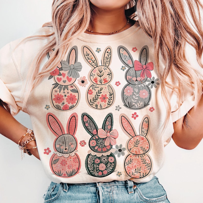 May include: A white t-shirt with a floral design featuring six bunnies with pink accents. The bunnies are surrounded by small flowers and leaves.