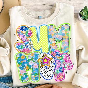May include: A cream colored sweatshirt with the word "SUMMER" written in large, colorful letters. The letters are decorated with a floral pattern and other colorful designs.