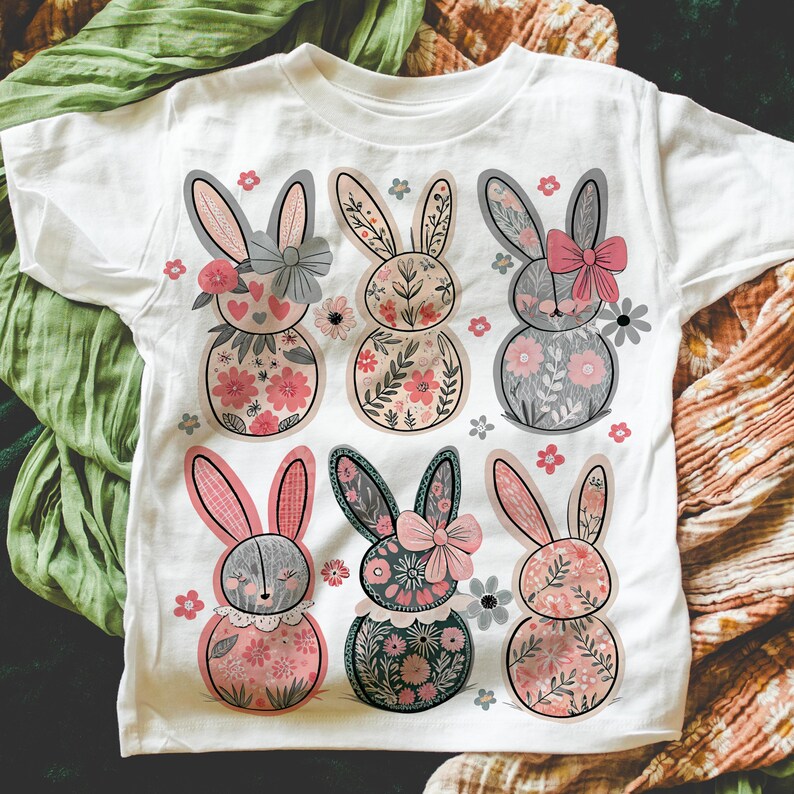 May include: White t-shirt with a floral pattern of six bunnies wearing bows. The bunnies are pink, gray, and green.