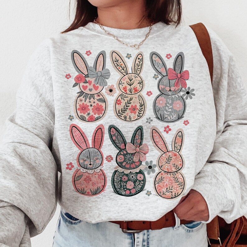May include: A gray sweatshirt with a floral pattern of six bunnies. The bunnies are all different colors and have different floral patterns on their bodies. The sweatshirt has a crew neck and long sleeves.
