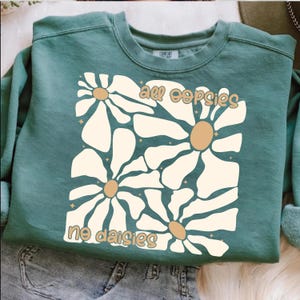 May include: Teal blue sweatshirt with a white daisy graphic and the text "all oopsies no daisies" in brown.