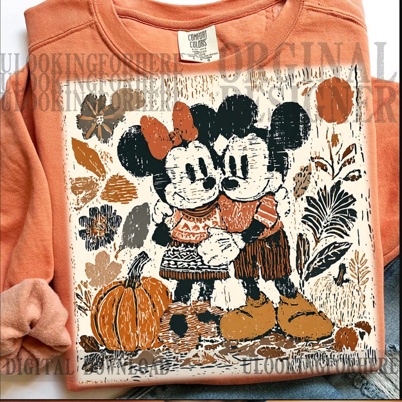 May include: Orange Comfort Colors sweatshirt with a graphic of Mickey and Minnie Mouse embracing, surrounded by autumn-themed elements like pumpkins and leaves. The design uses a rustic, vintage style with warm colours.
