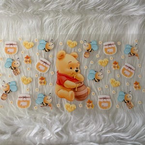 May include: A whimsical design featuring Winnie the Pooh, surrounded by bees, honey pots, and flowers. Pooh is wearing a red shirt and holding a honey pot. The design has a cartoon style and a light color palette.