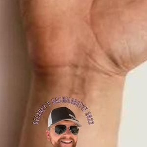 Pode incluir: Um close-up da m&atilde;o de uma pessoa com uma tatuagem tempor&aacute;ria que diz "Delaney's Bachelorette 2022" com uma foto de um homem usando &oacute;culos de sol e um chap&eacute;u. O texto abaixo da imagem diz "#shefoundawinner".