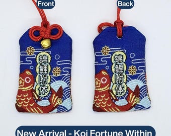 May include: Two blue fabric omamori charms featuring an embroidered red koi fish, white wave patterns, and gold floral accents. Each charm has a red cord and the text 锦鲤附体. The left charm includes a small gold bell. The text New Arrival - Koi Fortune Within is below.