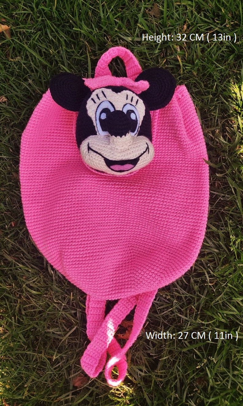 May include: Pink crocheted backpack with a Minnie Mouse face. The backpack measures 13 inches tall and 11 inches wide.