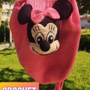 May include: A pink crocheted backpack with a Minnie Mouse face on the front. The backpack has a black bow and black ears. The text "CROCHET BAG PATTERN" is on a colorful background in the bottom left corner of the image.