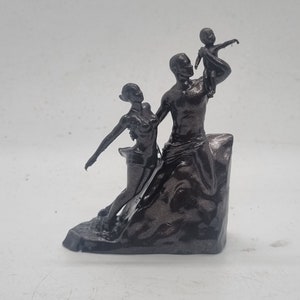 May include: A black and silver 3D printed sculpture of a family. The sculpture depicts a man holding a child in the air, a woman standing next to him, and a rocky base.