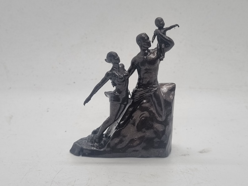 May include: A black and silver 3D printed sculpture of a family. The sculpture depicts a man holding a child in the air, a woman standing next to him, and a rocky base.