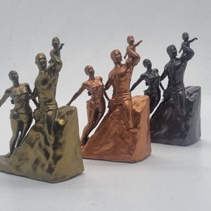 May include: Three bronze-colored sculptures of families, each with a parent holding a child. The sculptures are on a textured base and are arranged in a row from left to right.
